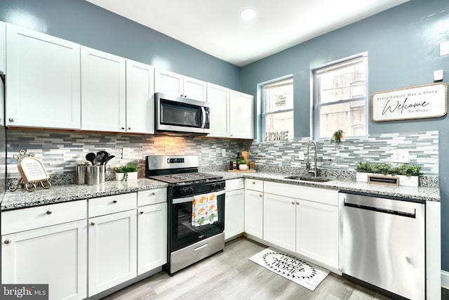 kitchen featuring stainless steel appliances, light stone countertops, sink, and white cabinets