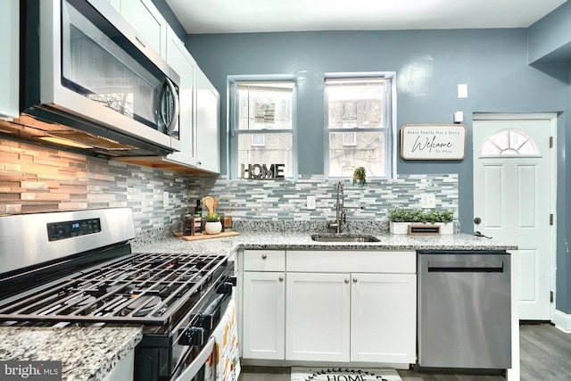 kitchen with sink, tasteful backsplash, appliances with stainless steel finishes, light stone countertops, and white cabinets