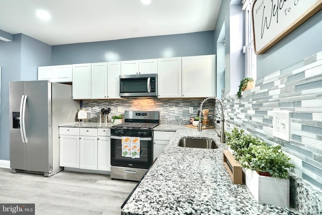 kitchen with appliances with stainless steel finishes, white cabinetry, sink, decorative backsplash, and light stone counters