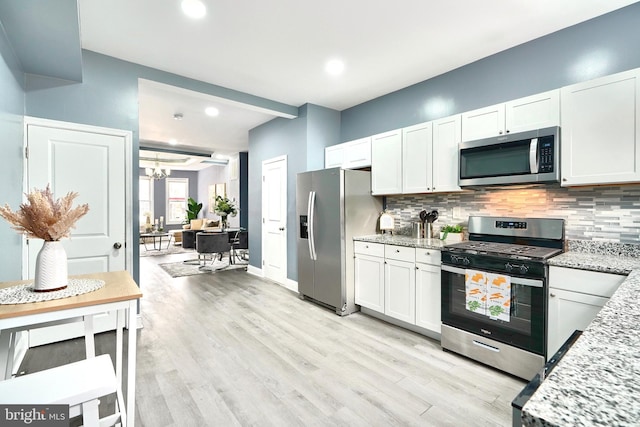 kitchen with stainless steel appliances, white cabinetry, light stone counters, and decorative backsplash