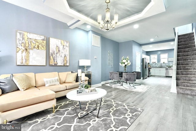 living room with wood-type flooring, a raised ceiling, and a notable chandelier