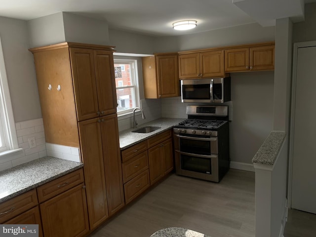 kitchen featuring light stone countertops, appliances with stainless steel finishes, decorative backsplash, sink, and light wood-type flooring