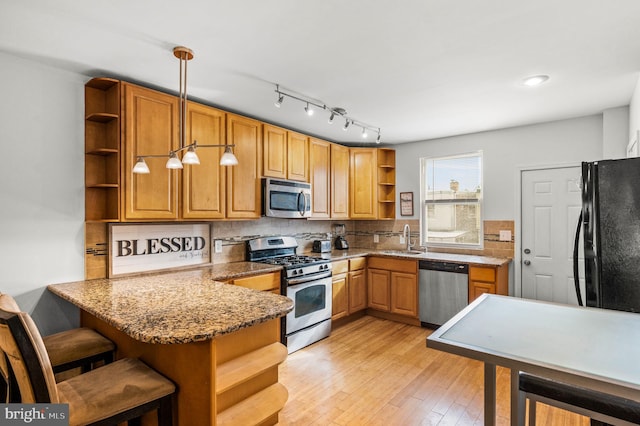 kitchen featuring kitchen peninsula, stone countertops, hanging light fixtures, sink, and stainless steel appliances