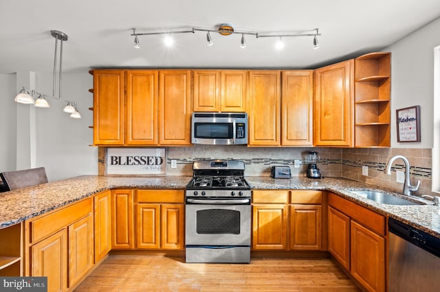 kitchen with hanging light fixtures, appliances with stainless steel finishes, sink, light stone countertops, and light hardwood / wood-style floors