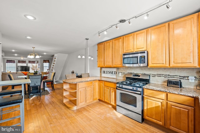 kitchen with decorative light fixtures, appliances with stainless steel finishes, kitchen peninsula, and a notable chandelier