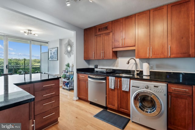 kitchen with washer / dryer, dark stone countertops, light hardwood / wood-style floors, sink, and stainless steel dishwasher