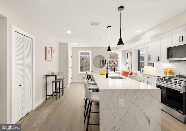 kitchen with sink, decorative light fixtures, light stone counters, electric range, and a center island with sink