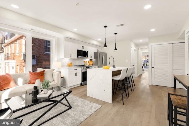 kitchen with white cabinets, appliances with stainless steel finishes, decorative light fixtures, an island with sink, and a breakfast bar area