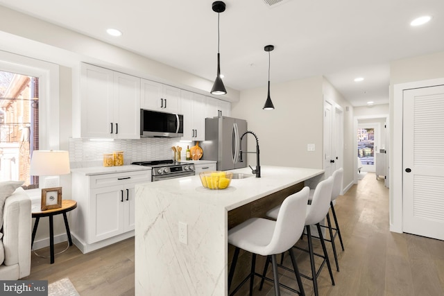 kitchen featuring white cabinets, stainless steel appliances, hanging light fixtures, and a kitchen island with sink