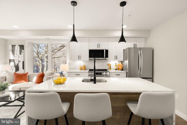 kitchen featuring hanging light fixtures, sink, white cabinetry, a center island with sink, and stainless steel appliances