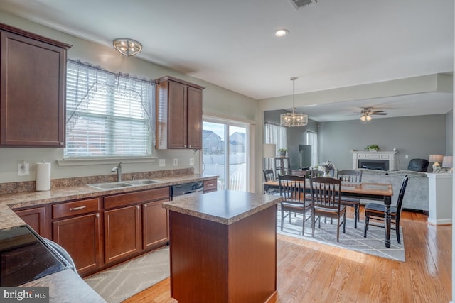 kitchen with a fireplace, a sink, light wood-type flooring, a center island, and decorative light fixtures