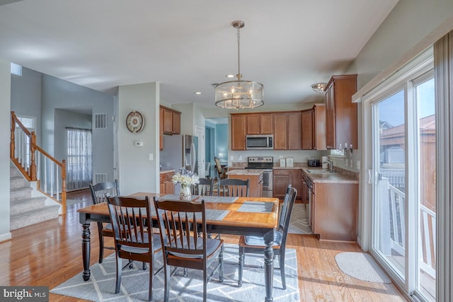 dining space with light wood-style flooring, stairway, visible vents, and a notable chandelier