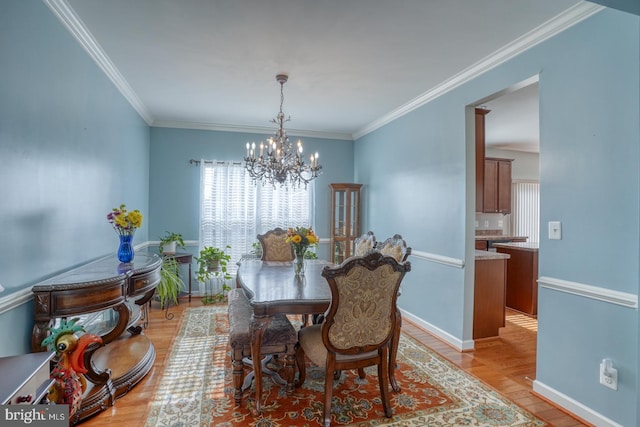 dining space featuring crown molding, baseboards, light wood-style flooring, and a notable chandelier