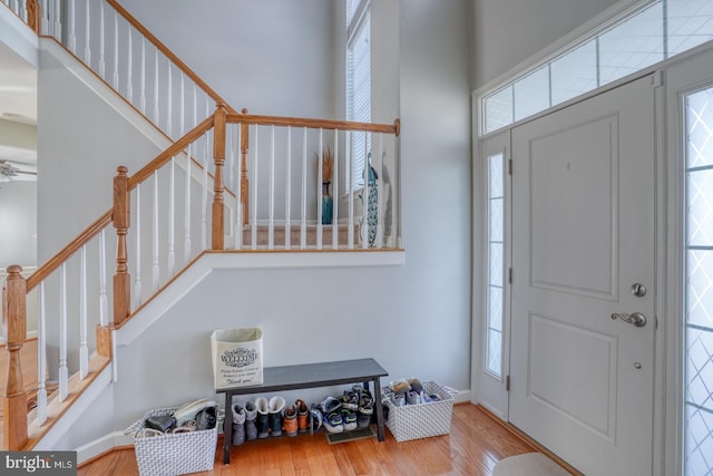 foyer entrance with stairs, a healthy amount of sunlight, a towering ceiling, and wood finished floors