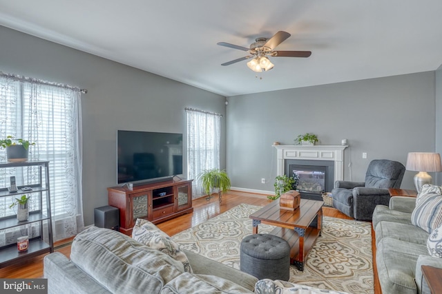 living room with baseboards, a ceiling fan, wood finished floors, and a glass covered fireplace