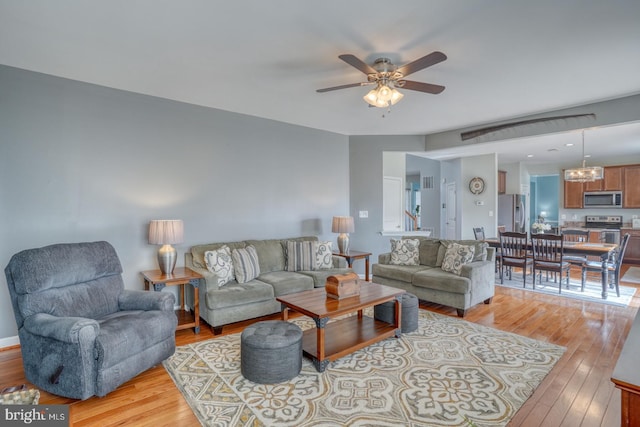 living area with ceiling fan with notable chandelier and light wood finished floors