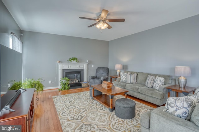 living area featuring hardwood / wood-style floors, a fireplace with flush hearth, a ceiling fan, and baseboards