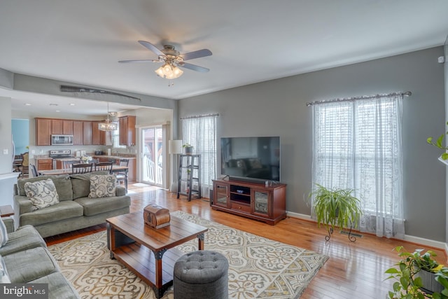 living room with light wood-style floors, ceiling fan, and baseboards