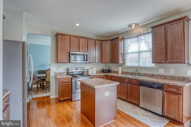 kitchen featuring stainless steel appliances, light wood finished floors, a kitchen island, and a sink