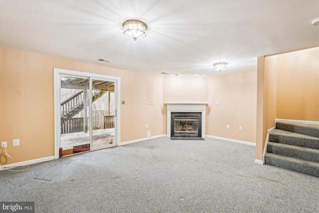 unfurnished living room with visible vents, baseboards, a fireplace with flush hearth, stairs, and carpet floors