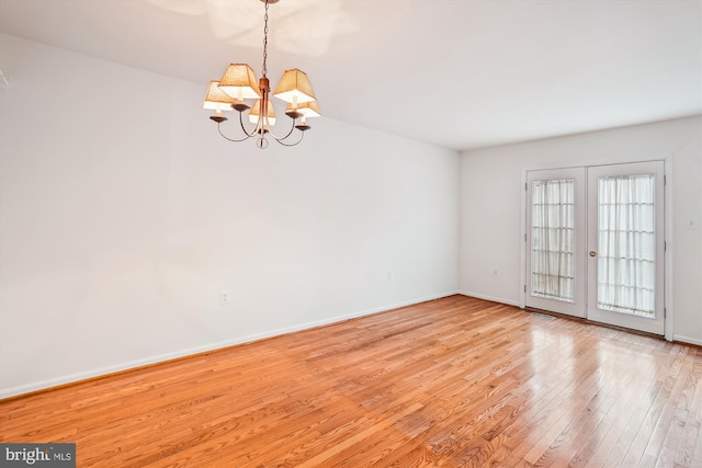 unfurnished room featuring an inviting chandelier, wood-type flooring, baseboards, and french doors