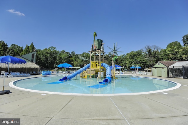 community pool featuring a water slide, playground community, fence, a water play area, and a patio area