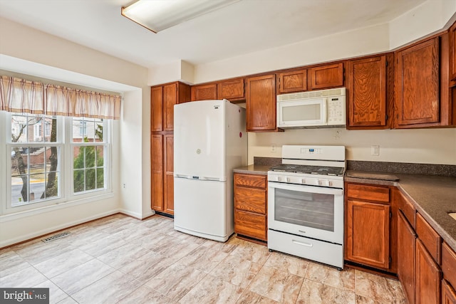 kitchen featuring dark countertops, white appliances, visible vents, and brown cabinets