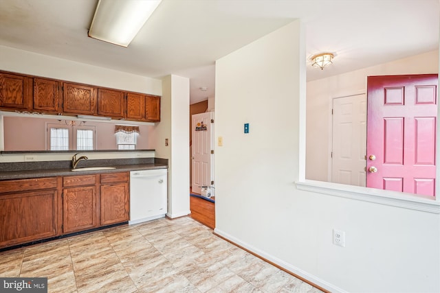 kitchen with dark countertops, brown cabinetry, a sink, dishwasher, and baseboards