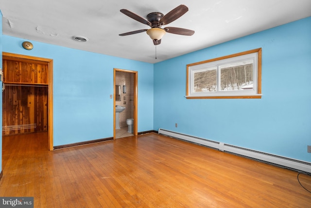 unfurnished bedroom featuring connected bathroom, a baseboard heating unit, ceiling fan, light wood-type flooring, and a closet