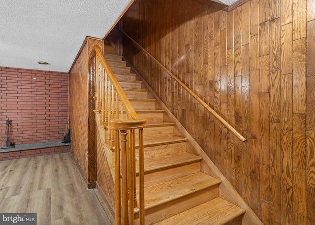 stairway with wood-type flooring, a textured ceiling, and wooden walls