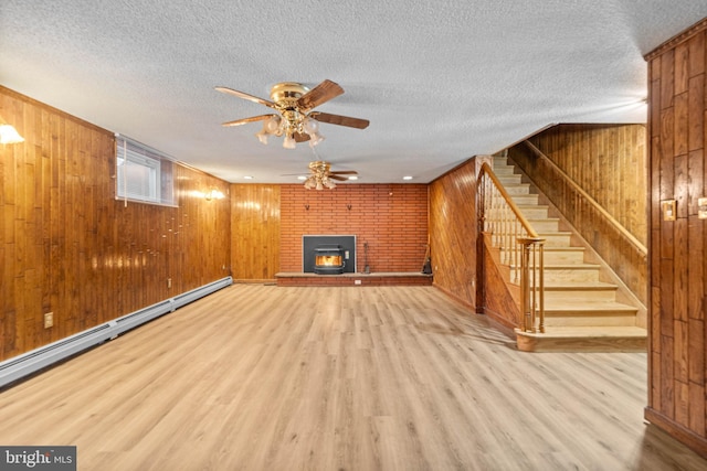 unfurnished living room with wooden walls, light wood-type flooring, a textured ceiling, and a baseboard heating unit