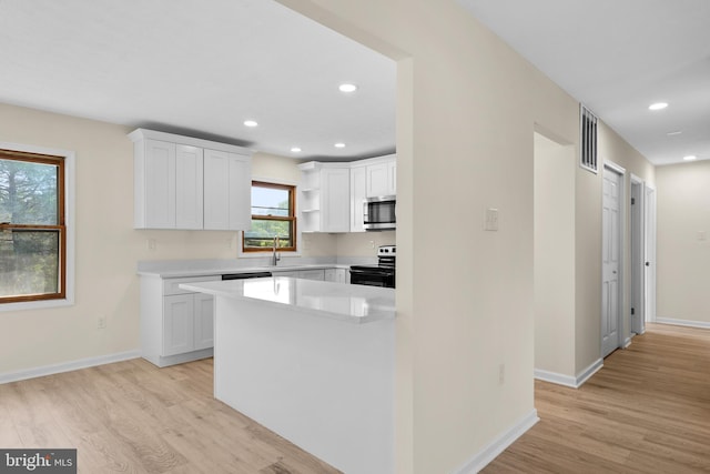 kitchen with white cabinetry, appliances with stainless steel finishes, a kitchen island, and light wood-type flooring