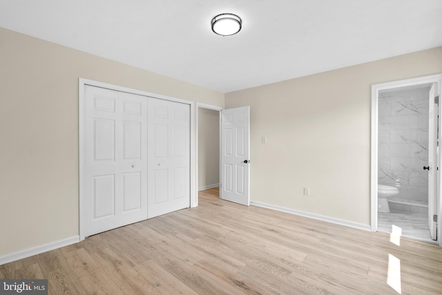 unfurnished bedroom featuring ensuite bath, a closet, and light wood-type flooring