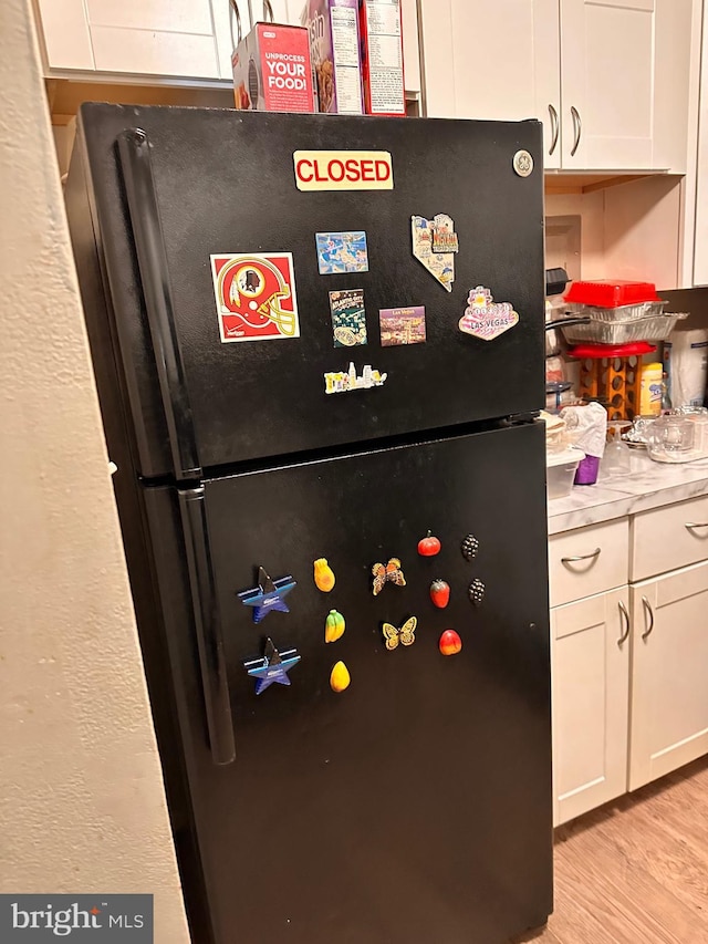 interior details with black refrigerator, white cabinetry, and light hardwood / wood-style flooring