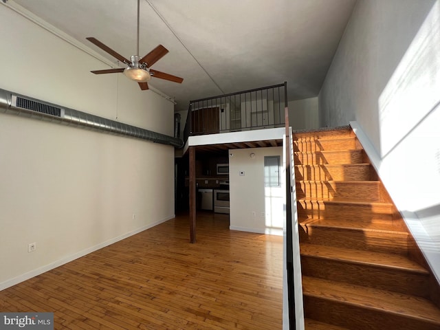 stairs featuring visible vents, a towering ceiling, ceiling fan, baseboards, and hardwood / wood-style flooring