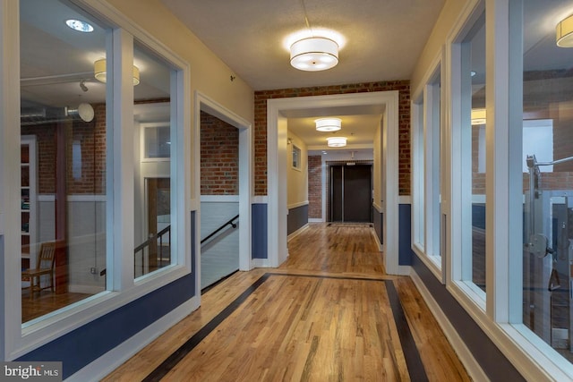 corridor featuring brick wall, wood finished floors, and baseboards