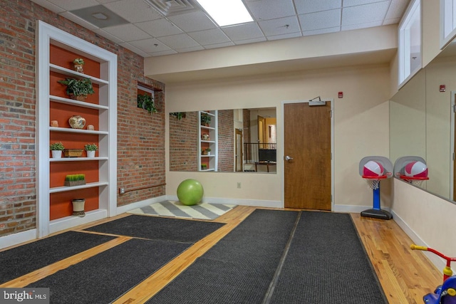 exercise area with brick wall, built in shelves, baseboards, and wood finished floors