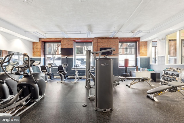 exercise room with brick wall and a textured ceiling