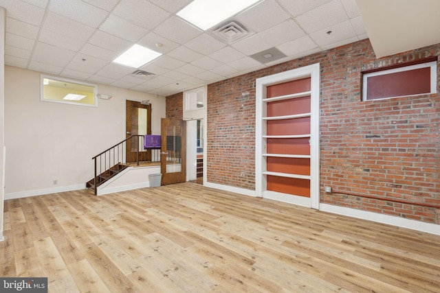 spare room with brick wall, wood-type flooring, built in shelves, and visible vents