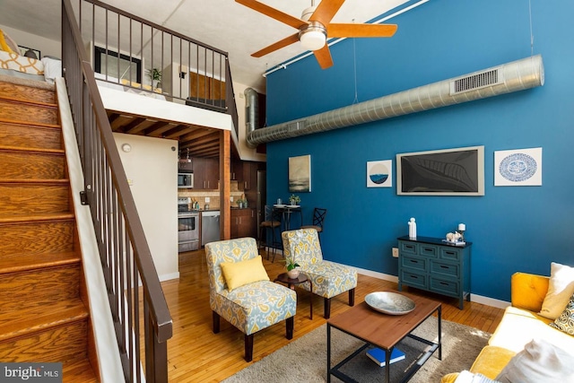 living area featuring baseboards, visible vents, a ceiling fan, stairway, and wood finished floors