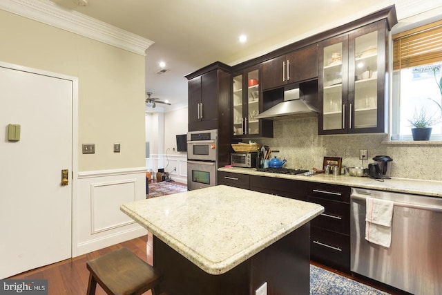 kitchen with wall chimney range hood, stainless steel appliances, a kitchen breakfast bar, and a center island