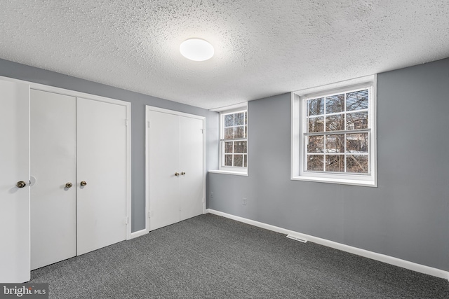 unfurnished bedroom with multiple closets, dark carpet, and a textured ceiling