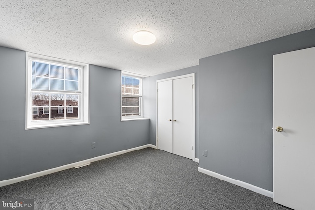 unfurnished bedroom featuring dark carpet, a closet, and a textured ceiling