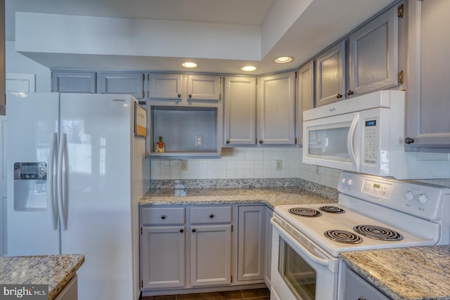 kitchen featuring light stone counters, white appliances, gray cabinets, and decorative backsplash