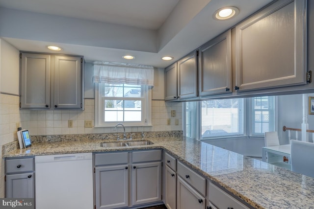 kitchen featuring sink, backsplash, light stone countertops, and dishwasher