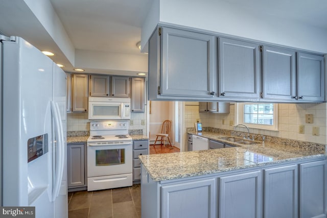 kitchen with tasteful backsplash, sink, light stone counters, kitchen peninsula, and white appliances