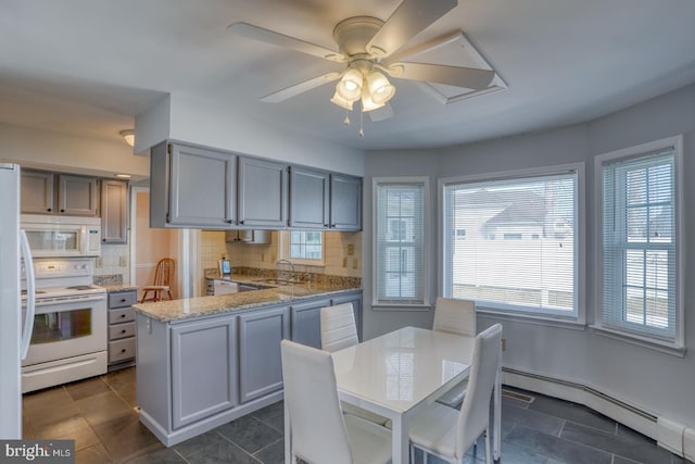 kitchen with sink, a baseboard heating unit, white appliances, light stone countertops, and backsplash