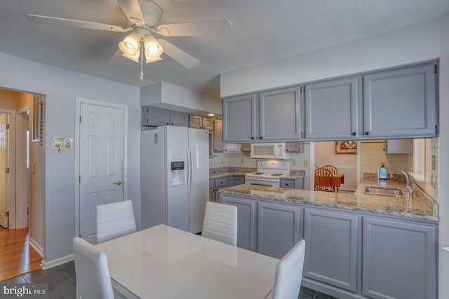 kitchen featuring sink, decorative backsplash, light stone counters, kitchen peninsula, and white appliances