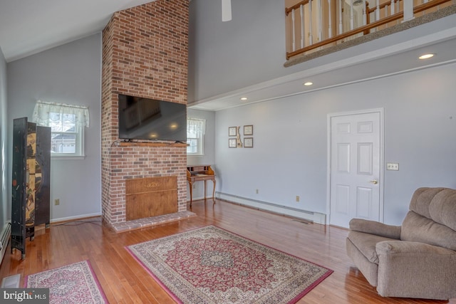 living room featuring hardwood / wood-style flooring, a fireplace, high vaulted ceiling, and a baseboard heating unit