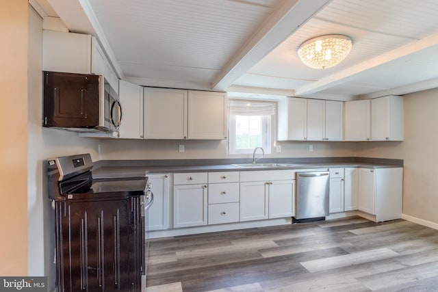 kitchen featuring appliances with stainless steel finishes, white cabinetry, sink, light wood-type flooring, and beam ceiling